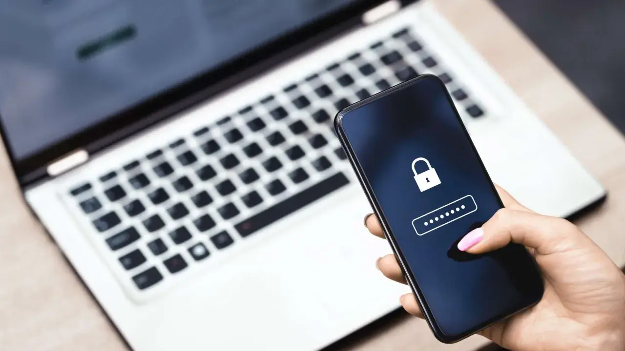 Hand hält Smartphone mit Schloss-Symbol und Passwort-Feld. Ein Laptop im Hintergrund erinnert an ein mögliches **Datenleck** und die Wichtigkeit eines sicheren **Passworts**.