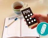 Hand hält Smartphone mit "PIN" und Punkten. Daneben ein Notizbuch mit Stift und eine Tasse Tee. Was ist ein PIN?