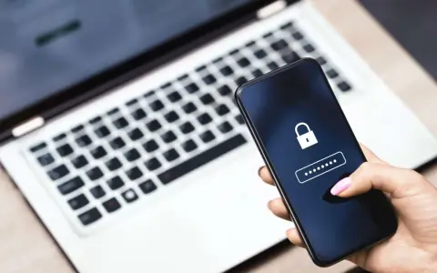 Hand hält Smartphone mit Schloss-Symbol und Passwort-Feld. Ein Laptop im Hintergrund erinnert an ein mögliches **Datenleck** und die Wichtigkeit eines sicheren **Passworts**.