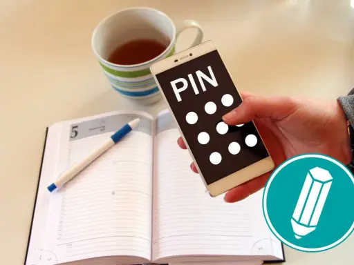 Hand hält Smartphone mit "PIN" und Punkten. Daneben ein Notizbuch mit Stift und eine Tasse Tee. Was ist ein PIN?